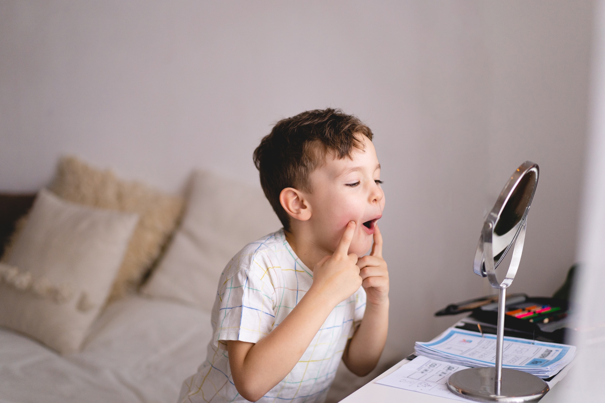 Boy pronouncing sound O looking at mirror doing an online Speech therapy lesson through a laptop