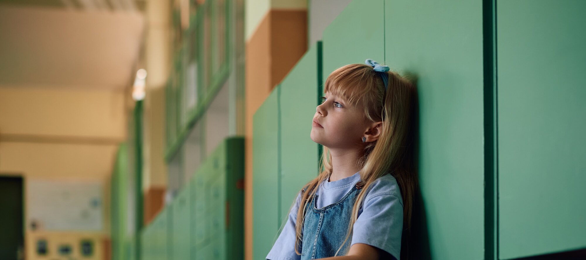 Pensive little girl sitting alone at school hallway.